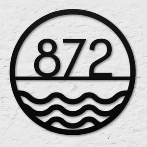 May include: Black metal house number sign with the number 872 in a circle with a wave design at the bottom.
