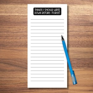 May include: A white notepad with horizontal lines and the text "THINGS I SHOULD WRITE DOWN BEFORE I FORGET" in a black rectangle. A blue pen rests diagonally across the notepad.