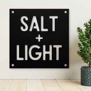 May include: Black metal sign with white lettering that reads "SALT + LIGHT".