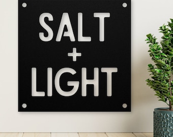 May include: Black metal sign with white lettering that reads "SALT + LIGHT".