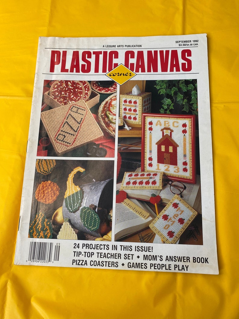 May include: A magazine cover for Plastic Canvas Corner, a leisure arts publication. The cover features a variety of plastic canvas projects, including a pizza box, a tissue box cover, a schoolhouse, and a set of gourds. The text on the cover reads "24 Projects in this Issue! Tip-Top Teacher Set, Mom's Answer Book, Pizza Coasters, Games People Play."