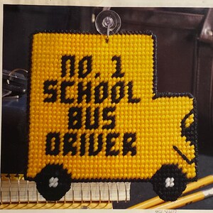 May include: A yellow and black crocheted sign shaped like a school bus with the text "No 1 School Bus Driver".