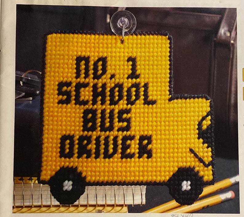 May include: A yellow and black crocheted sign shaped like a school bus with the text "No 1 School Bus Driver".