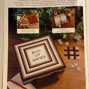 May include: A brown and white canvas box with the words "BOX OF GAMES" embroidered on the front. The box is open and shows a variety of games, including dominoes, checkers, tic-tac-toe, and backgammon.