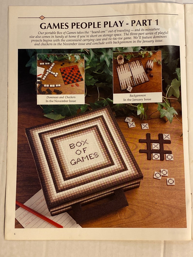 May include: A brown and white canvas box with the words "BOX OF GAMES" embroidered on the front. The box is open and shows a variety of games, including dominoes, checkers, tic-tac-toe, and backgammon.