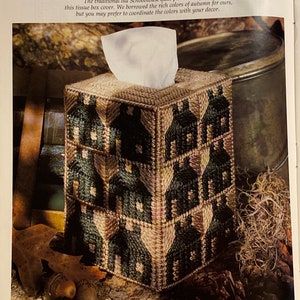 May include: A green and brown tissue box cover with a schoolhouse pattern. The cover is made of fabric and has a quilted design. The text "SCHOOLHOUSE BOUTIQUE" is printed on the cover.