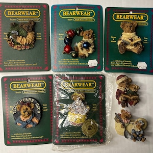 Puede incluir: Una colección de seis pines coleccionables con varios personajes de Boyds Bears and Friends. Los pines se muestran en tarjetas verdes y blancas con el texto "BEARWEAR" y "Boyds Bears and Friends". Los pines presentan una variedad de temas, incluyendo Navidad, osos de peluche y animales del bosque.
