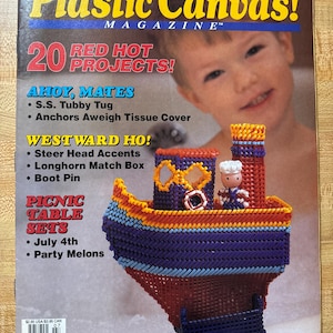 Può includere: La copertina della rivista "Plastic Canvas!" presenta un'imbarcazione artigianale in tela di plastica colorata. La copertina include il testo per "20 Red Hot Projects!" e titoli di progetti come "S.S. Tubby Tug" e "July 4th". Un bambino è visibile sullo sfondo.