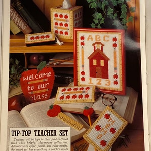 May include: A set of five red and yellow canvas needlepoint crafts with an apple theme. The set includes a tissue box cover, a pencil holder, a ruler, a small box, and a framed picture. The picture features a red schoolhouse with the letters ABC and the numbers 123. The pencil holder has the words "Welcome to our class".