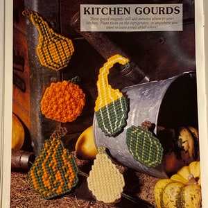 May include: A set of six colorful gourd-shaped magnets with a green, orange, and yellow color scheme. The magnets are arranged on a rustic background with a metal bucket and gourds. "Kitchen Gourds" is written in the image.