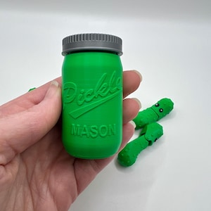 May include: A green glass jar with a gray lid. The jar has the word "Pickle" and "MASON" embossed on the front.
