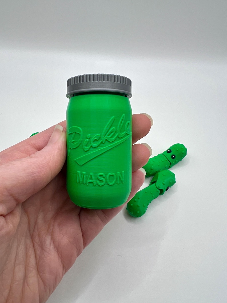 May include: A green glass jar with a gray lid. The jar has the word "Pickle" and "MASON" embossed on the front.