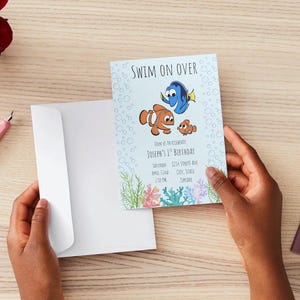 May include: A light blue invitation card with the text "Swim on Over" and cartoon fish illustrations. The invitation includes event details for Joseph's 1st birthday. A white envelope is open next to the card.