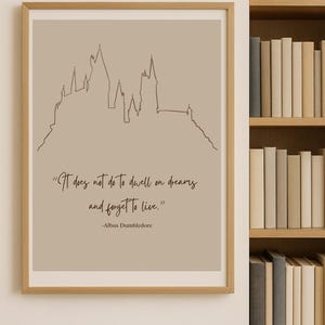 以下が含まれることがあります： ベージュの背景に城のシルエットの線画が描かれた、額入りのアートプリントです。「It does not do to dwell on dreams and forget to live.」というアルバス・ダンブルドアの引用句が手書き風のフォントで表示されています。フレームはライトブラウンです。