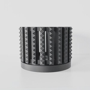 May include: A black cylindrical planter with a geometric design. The planter has a series of triangular shapes that create a unique and modern look.