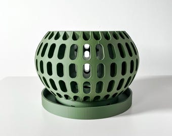 May include: A green, spherical planter with a perforated design. The planter sits on a matching round base. The openwork design allows for air circulation and drainage, making it suitable for various plants. The planter is made of a solid material.