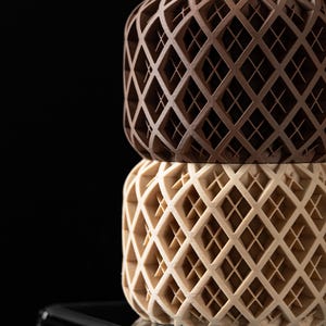 May include: Two stacked cylindrical containers with a geometric lattice pattern. The top container is brown and the bottom container is beige.