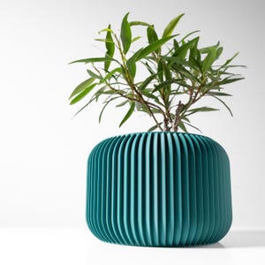 May include: A teal green planter with a ribbed design, featuring a green leafy plant growing inside.