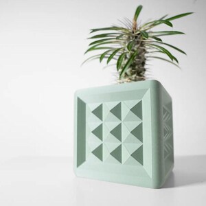 May include: A light green geometric planter with a triangular pattern. A small succulent plant is growing inside the planter.