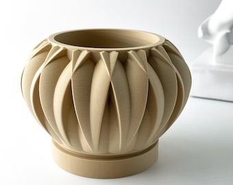 May include: A beige ceramic planter with a unique geometric design. The planter has a wide, round base and a slightly flared top. The design features a series of overlapping, curved lines that create a textured, almost organic look.