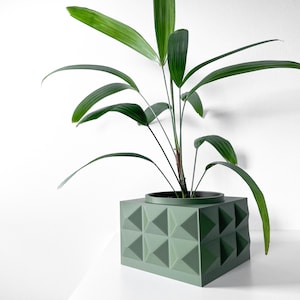 May include: A green geometric planter with a houseplant. The planter has a square shape with a textured surface.