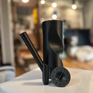 May include: Black watering can with a long spout and a round, perforated watering head. The watering can has a twisted design.