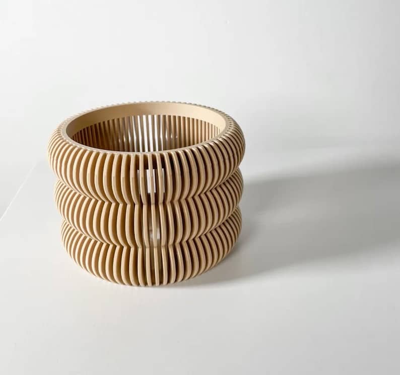 May include: A beige wooden planter with a unique, layered design. The planter is made of thin, curved slats that create a geometric pattern.