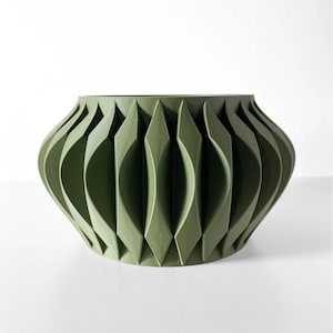 May include: A green ceramic planter with a geometric, folded design. The planter has a wide, round base and a slightly narrower opening.
