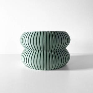 May include: A light green ceramic planter with a unique ribbed design. The planter has two sections, creating a rounded, hourglass shape.