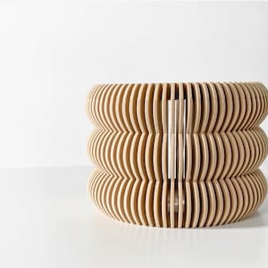 May include: A light brown wooden lampshade with a unique, wavy design. The lampshade is made of thin, overlapping strips of wood that create a three-dimensional effect.