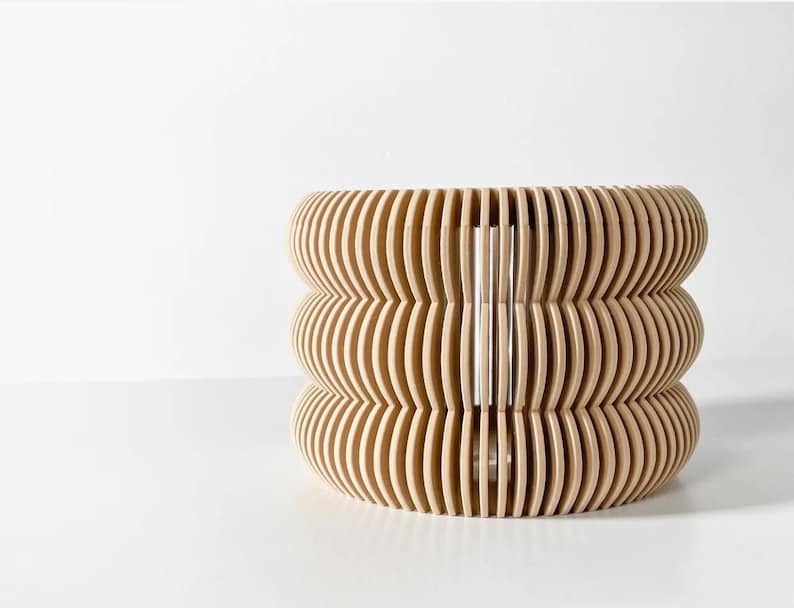 May include: A light brown wooden lampshade with a unique, wavy design. The lampshade is made of thin, overlapping strips of wood that create a three-dimensional effect.
