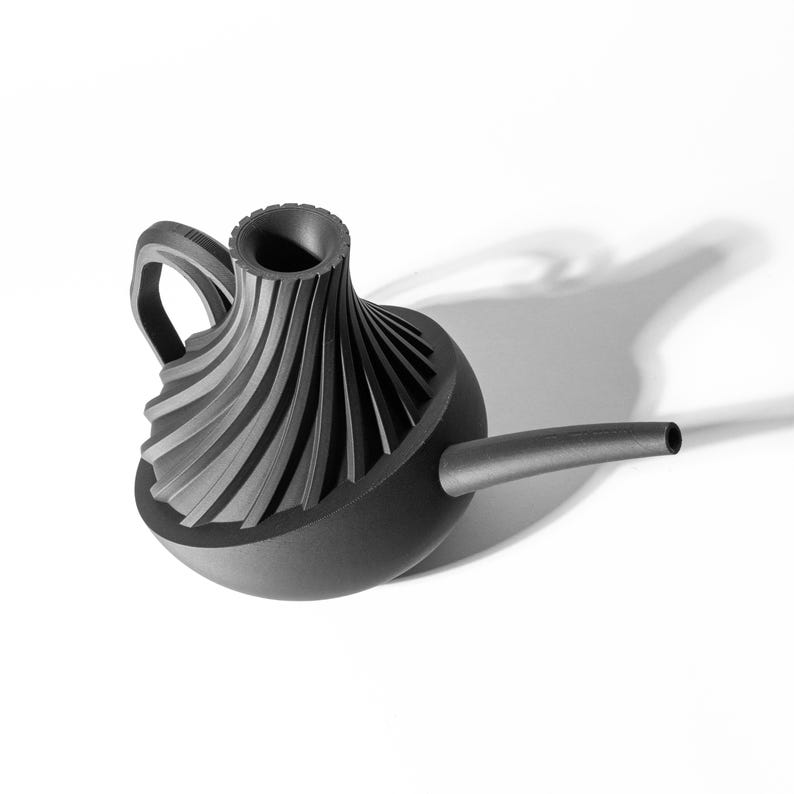 May include: A black watering can with a unique, geometric design. The spout is long and curved, and the handle is attached to the side of the can.