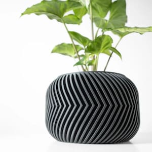 May include: A dark gray planter with a geometric chevron pattern. The planter is made of a textured material and has a rounded shape. A green plant is growing inside the planter.
