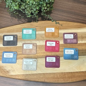 May include: A wooden board with 14 small square color samples. The samples are labeled with names like "Copper Brown", "Yellow Shimmer", and "Cobalt Blue Metallic".