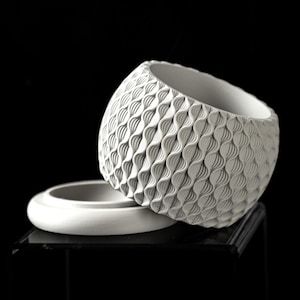 May include: A white ceramic planter with a textured, wave-like design. The planter has a removable lid.