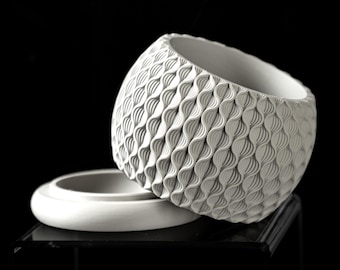 May include: A white ceramic planter with a textured, wave-like design. The planter has a removable lid.