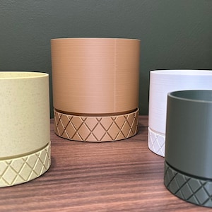 May include: Four different colored plant pots with a geometric pattern on the bottom. The pots are made of a textured material and are in various shades of brown, green, white, and yellow.