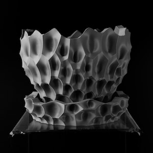 May include: A grayscale, honeycomb-patterned bowl with a matching base. The bowl's exterior features a textured, cellular design, and the base is a clear, geometric shape. The background is solid black, highlighting the bowl's intricate details.