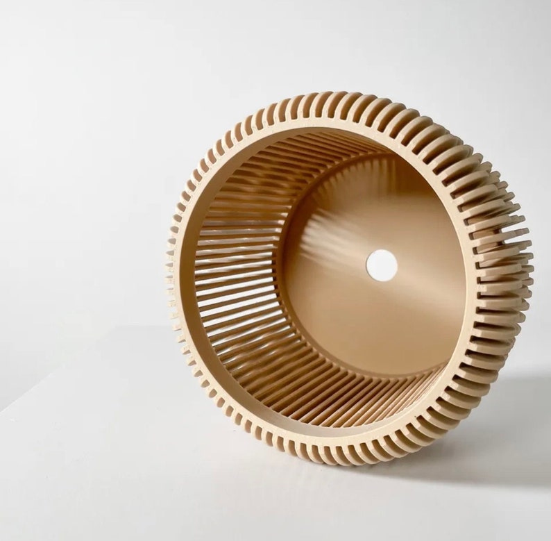 May include: A beige, round, decorative planter with a slatted design. The planter has a hole in the bottom for drainage.