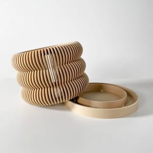 May include: A set of three beige, wooden, round, decorative containers with a wavy, ribbed design. The containers are stacked on top of each other.