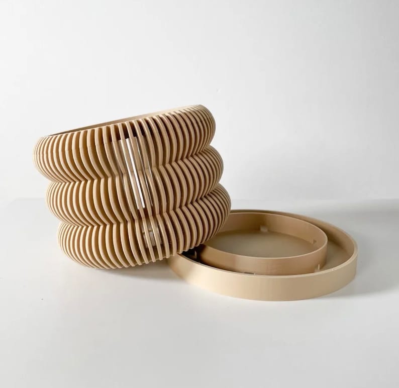 May include: A set of three beige, wooden, round, decorative containers with a wavy, ribbed design. The containers are stacked on top of each other.