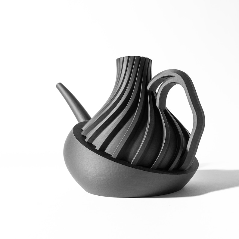 May include: A black ceramic watering can with a unique, folded design. The spout is long and curved, and the handle is a single, continuous loop.