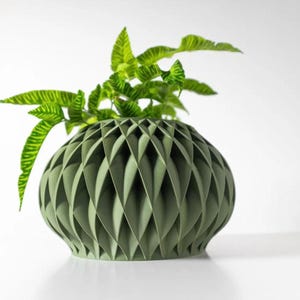 May include: A green ceramic vase with a geometric pattern. The vase is filled with green leafy plants.