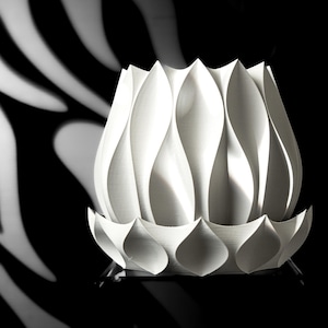 May include: A white ceramic vase with a unique, organic design. The vase has a wide, rounded base and a narrow opening at the top. The surface of the vase is textured with a series of overlapping, petal-like shapes.