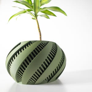 May include: A green, spherical planter with a spiral design, holding a small plant with green and yellow leaves. The planter has a series of angled, vertical openings. The plant pot is a decorative item for indoor use.