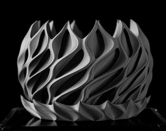 May include: A gray, 3D printed, decorative object with a geometric, wave-like pattern. The object is shaped like a bowl or a vase.