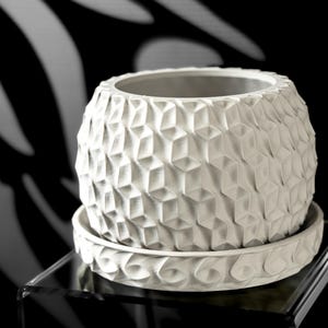 May include: White ceramic planter with a geometric pattern. The planter has a matching saucer.
