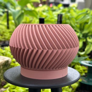 May include: A pink ceramic planter with a geometric design. The planter is sitting on a black tripod stand.