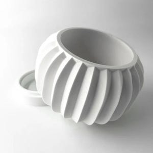 May include: White ceramic planter with a ribbed design. The planter has a round shape and a wide opening.