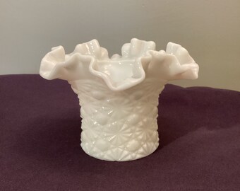 May include: A white, vintage-style glass vase with a ruffled rim. The vase has a textured, diamond-patterned exterior. The ruffled edge adds a delicate touch to the piece. This decorative vase is suitable for displaying small flowers or as a standalone accent.